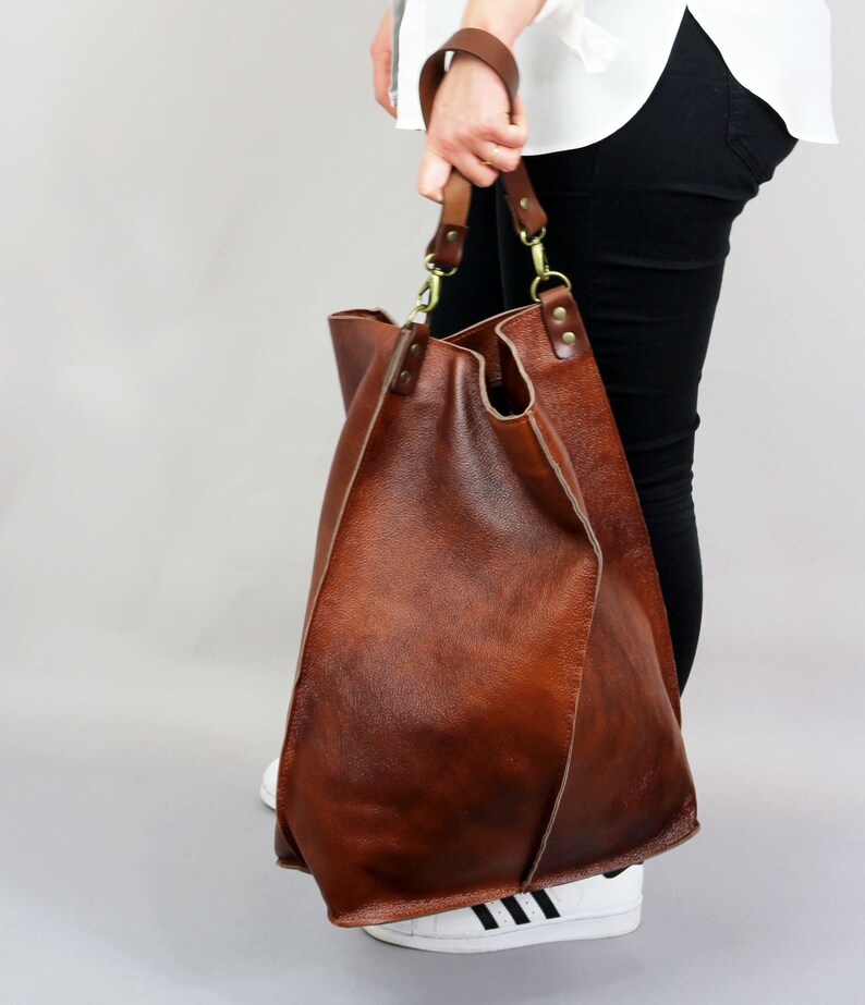May include: A large brown leather tote bag with a long strap. The bag has a slouchy, relaxed look and is made of high-quality leather.