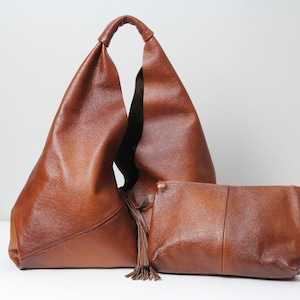 May include: A brown leather tote bag with a long tassel and a matching brown leather clutch.