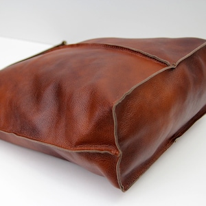 May include: A brown leather tote bag with a stitched edge. The bag has a simple design and is made of high-quality leather.