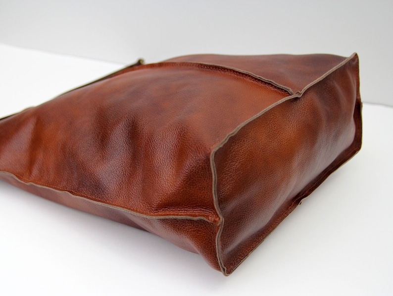 May include: A brown leather tote bag with a stitched edge. The bag has a simple design and is made of high-quality leather.