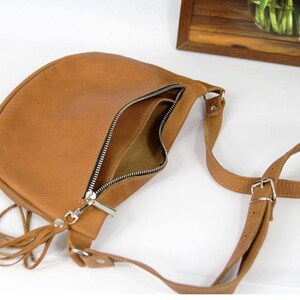 May include: A brown leather crossbody bag with a long strap and a tassel. The bag has a zipper closure and a flap.