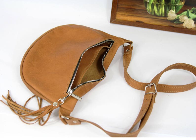 May include: A brown leather crossbody bag with a long strap and a tassel. The bag has a zipper closure and a flap.