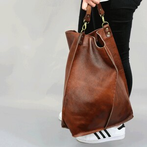 May include: A large brown leather tote bag with a long strap. The bag is made of soft, supple leather and has a slouchy, casual look.
