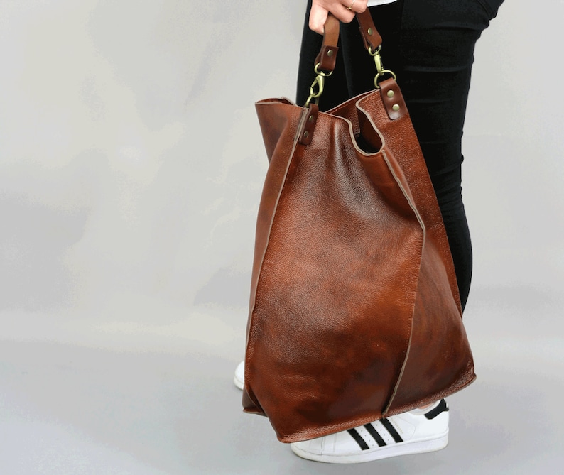 May include: A large brown leather tote bag with a long strap. The bag is made of soft, supple leather and has a slouchy, casual look.