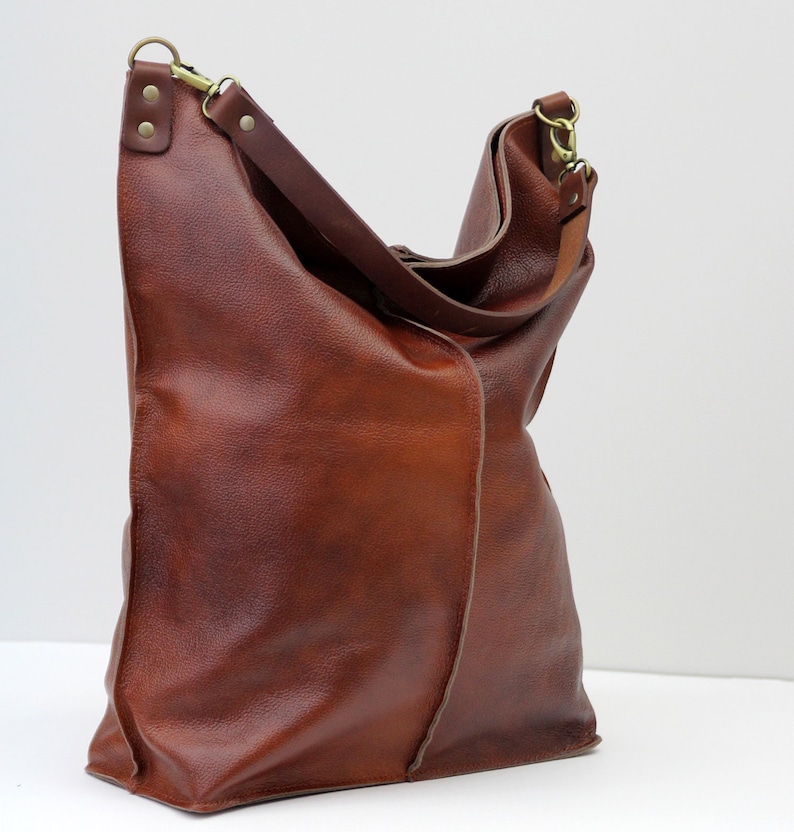 May include: A large brown leather tote bag with a long strap and a gold buckle. The bag has a slouchy, casual look.