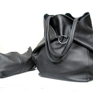 May include: Two black leather tote bags. The larger bag has a single ring on the top and two straps. The smaller bag has a zipper closure.