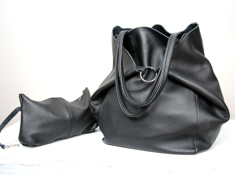May include: Two black leather tote bags. The larger bag has a single ring on the top and two straps. The smaller bag has a zipper closure.