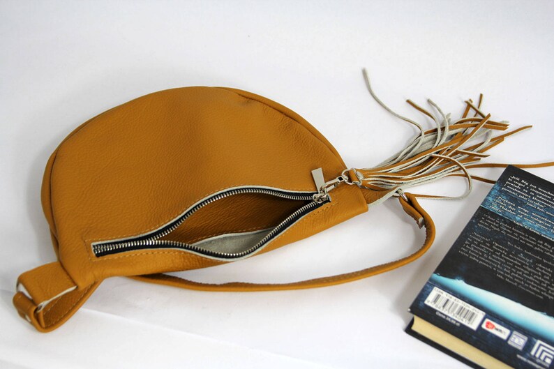 May include: A tan leather half-moon shaped crossbody bag with a zipper closure and a long fringe tassel.
