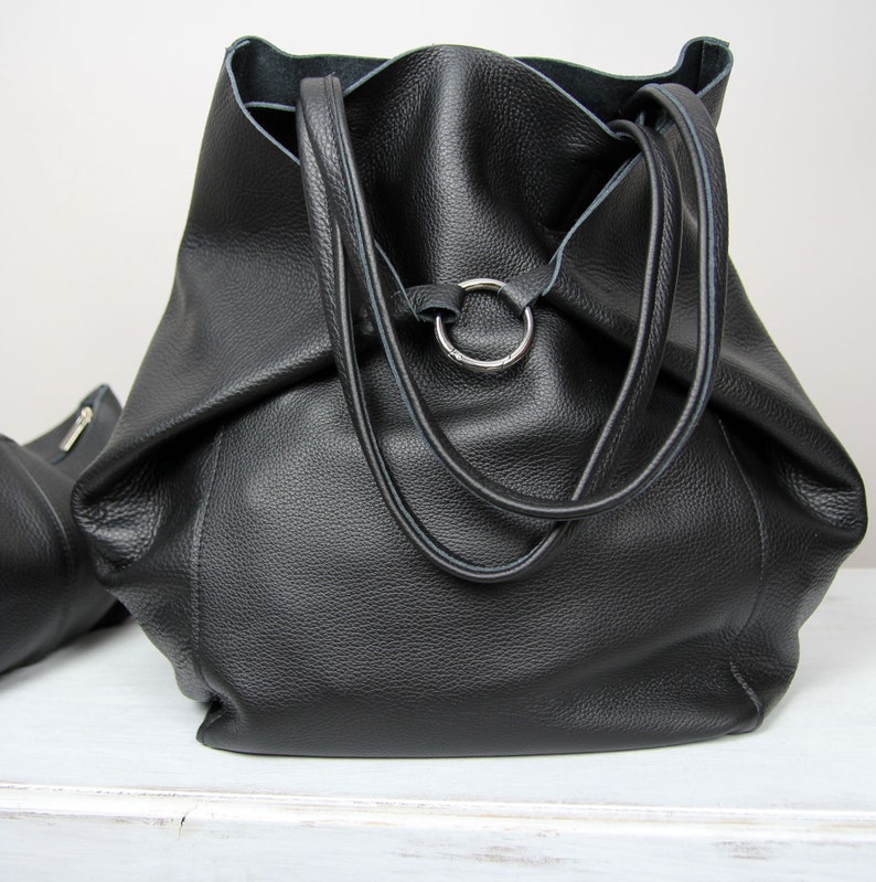 May include: A large black leather tote bag with two top handles and a silver ring detail.