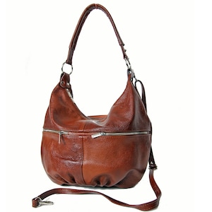 Pu&ograve; includere: Una borsa hobo in pelle marrone con una tracolla lunga e diverse tasche con cerniera.