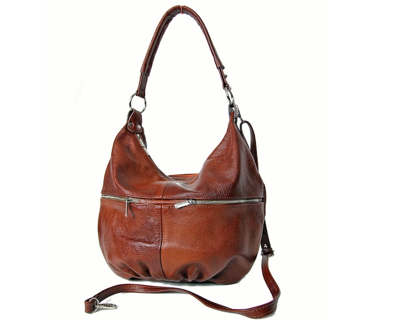 Pu&ograve; includere: Una borsa hobo in pelle marrone con una tracolla lunga e diverse tasche con cerniera.