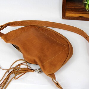 May include: A brown leather crossbody bag with a fringe detail and a silver zipper. The bag has a long adjustable strap.