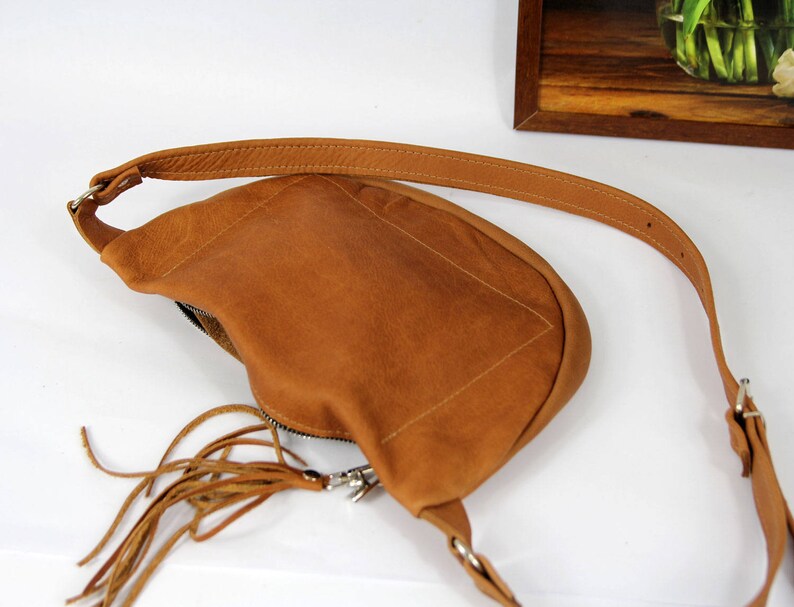 May include: A brown leather crossbody bag with a fringe detail and a silver zipper. The bag has a long adjustable strap.