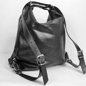 K&ouml;nnte beinhalten: Schwarzer Lederrucksack mit verstellbaren Schultergurten und silberfarbenen Metallbeschl&auml;gen. Die Tasche hat eine abgerundete Form und einen oberen Griff. Die Gurte sind mit Schnallen befestigt. Die Tasche ist aus strukturiertem Leder.