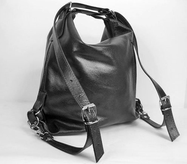 K&ouml;nnte beinhalten: Schwarzer Lederrucksack mit verstellbaren Schultergurten und silberfarbenen Metallbeschl&auml;gen. Die Tasche hat eine abgerundete Form und einen oberen Griff. Die Gurte sind mit Schnallen befestigt. Die Tasche ist aus strukturiertem Leder.