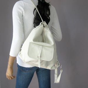 Puede incluir: Una mochila de cuero blanco con un bolsillo frontal grande y correas ajustables.