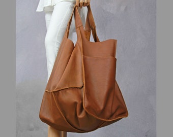 Pode incluir: Uma grande bolsa tote de couro marrom com um único bolso grande na frente. A bolsa tem um visual descontraído e sem estrutura e é feita de couro macio e flexível.