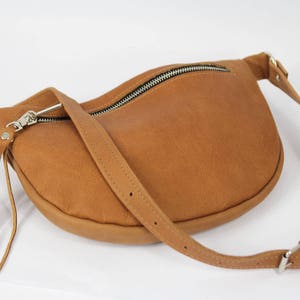 May include: A brown leather fanny pack with a zipper closure and a long fringe tassel. The bag has a long adjustable strap.