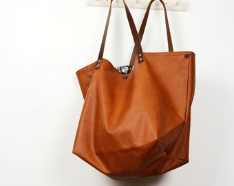 Könnte beinhalten: Eine große braune Ledertasche mit braunen Lederriemen. Die Tasche hängt an Haken an einer weißen Wand.