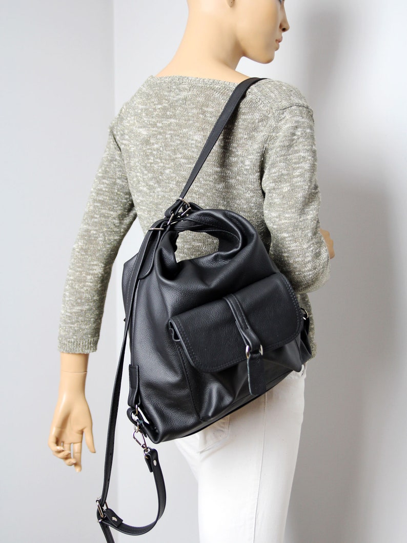 K&ouml;nnte beinhalten: Schwarzer Lederrucksack mit einer Klappentasche und verstellbaren Tr&auml;gern. Die Tasche hat ein weiches, l&auml;ssiges Design und silberfarbene Hardware. Der Rucksack wird &uuml;ber der Schulter getragen.