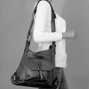 K&ouml;nnte beinhalten: Eine schwarze Leder-Umh&auml;ngetasche mit einer Klappentasche und verstellbaren Tr&auml;gern. Die Tasche hat eine strukturierte Oberfl&auml;che und einen Schnallenverschluss. Die Tasche wird &uuml;ber der Schulter getragen.
