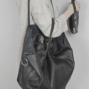 May include: A large black leather tote bag with a smaller black leather pouch attached to the side. The tote bag has a long strap and a top handle.