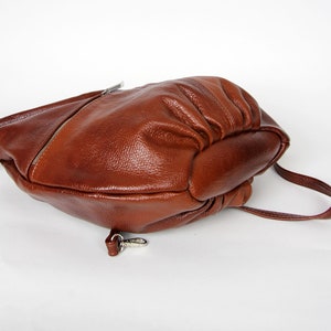 Pu&ograve; includere: Una borsa a tracolla in pelle marrone con un cinturino singolo e una fibbia argentata. La borsa &egrave; realizzata in pelle morbida e testurizzata e ha una forma leggermente arrotondata.