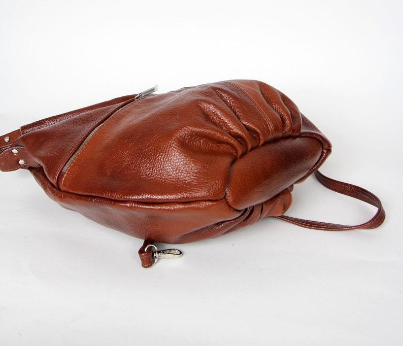 Pu&ograve; includere: Una borsa a tracolla in pelle marrone con un cinturino singolo e una fibbia argentata. La borsa &egrave; realizzata in pelle morbida e testurizzata e ha una forma leggermente arrotondata.