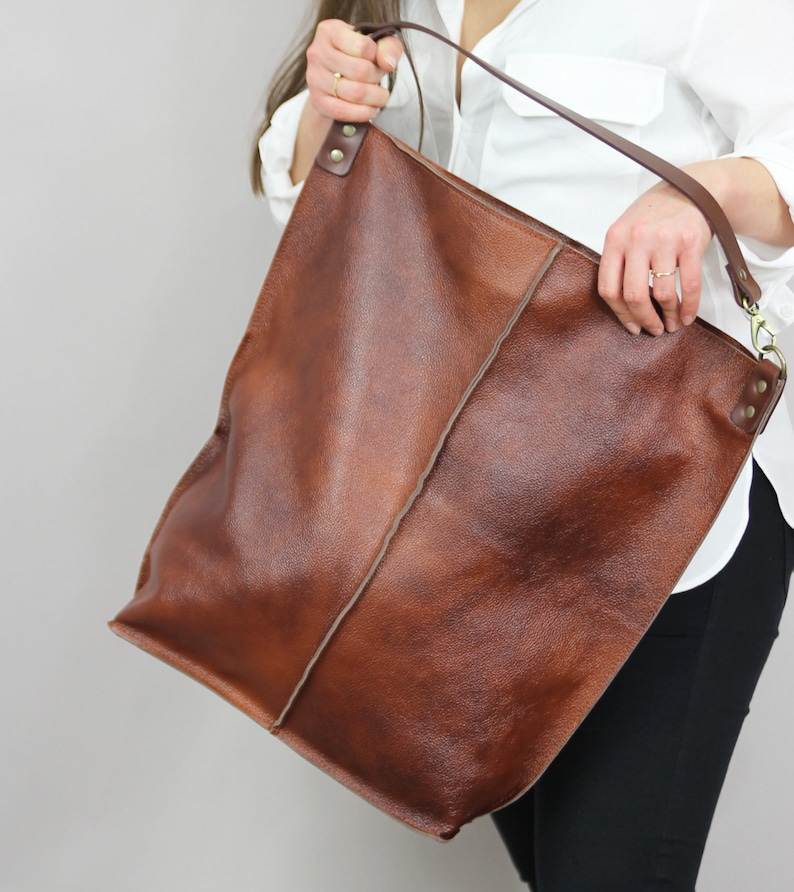 May include: A large brown leather tote bag with a long strap. The bag has a simple design and is made of high-quality leather.