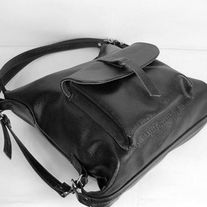 K&ouml;nnte beinhalten: Schwarzer Lederrucksack mit Klappenverschluss und verstellbaren Tr&auml;gern. Die Tasche hat eine strukturierte Oberfl&auml;che und einen einzelnen oberen Griff. Das Design umfasst silberfarbene Metallbeschl&auml;ge und eine Vordertasche unter der Klappe.