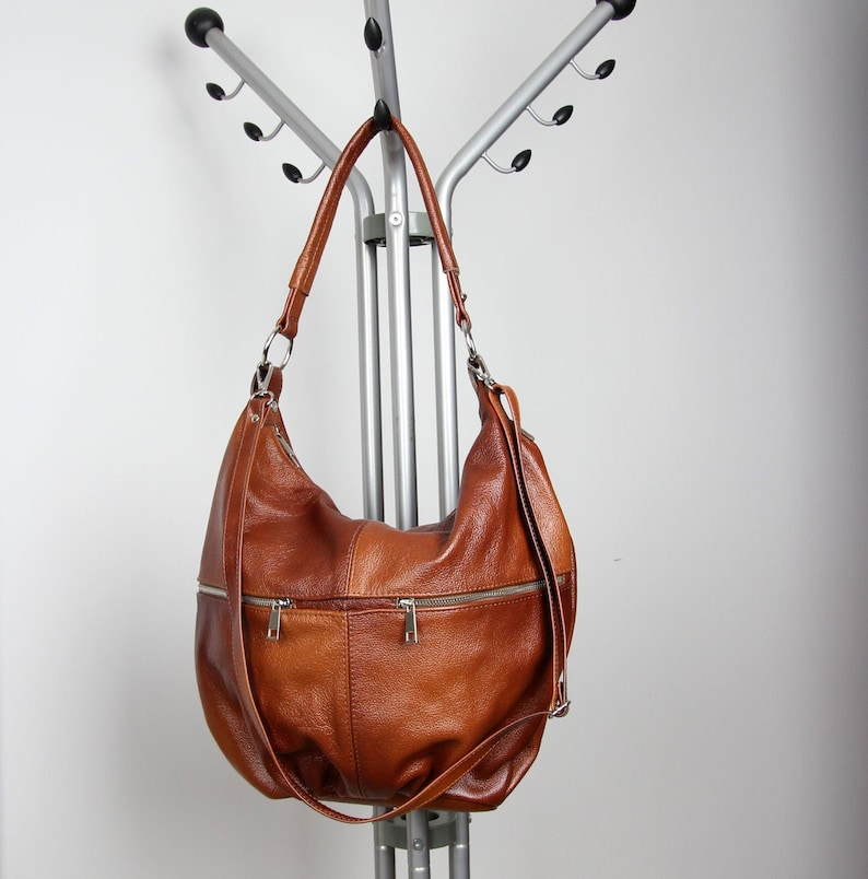 Pu&ograve; includere: Una borsa hobo in pelle marrone con una tracolla lunga e diversi scomparti con cerniera.