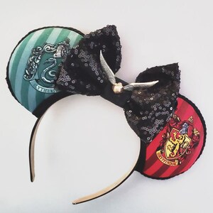 May include: A pair of black sequined mouse ears with a bow and golden snitch. One ear features a green and white striped design with a silver crest and the word "Slytherin". The other ear has a red and black striped design with a gold crest and the word "Gryffindor".