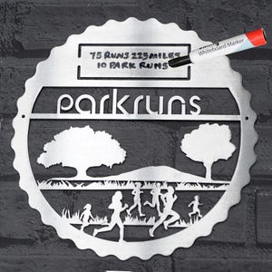 Peut inclure: Une plaque de parcrun en métal argenté avec un fond blanc et du texte noir. La plaque représente une silhouette de parc avec des arbres et des coureurs. Le texte sur la plaque indique "75 runs 225 miles 10 park runs" et "parkruns".