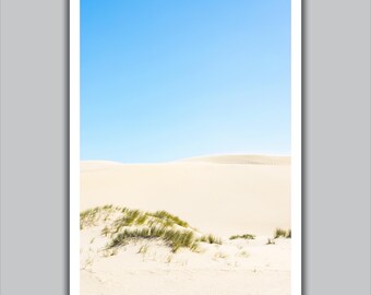 May include: A landscape photograph featuring a serene desert scene. The image showcases rolling sand dunes in shades of beige and tan, set against a clear, bright blue sky. Patches of green grass add contrast to the foreground, creating a sense of natural beauty.