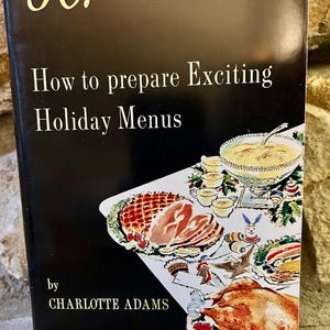 May include: A vintage cookbook titled "How to Prepare Exciting Holiday Menus" by Charlotte Adams. The cover is black with the title in white and features illustrations of holiday dishes. The book is part of the Vanderbilt Success Program for Women.