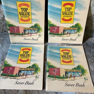Puede incluir: Cuatro libretas de ahorro vintage de Top Value Stamps. Cada libreta tiene un sello rojo, amarillo y blanco con las palabras "Top Value Stamps" impresas en él. Las libretas son marrones con un fondo blanco y presentan una ilustración de dibujos animados de una tienda con gente caminando frente a ella.