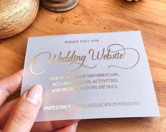 Op de afbeelding: Een witte kaart met gouden letters die "Bezoek onze trouwwebsite" zegt en het websiteadres "knot.com/raelandjacksonwedding" bevat.