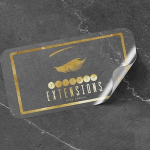 Peut inclure: Un autocollant doré avec un design stylisé de cils et le texte "EYELASH EXTENSIONS WIDE CHOICE".