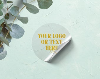 May include: A clear round sticker with a gold peel-back tab. The sticker has the text "YOUR LOGO OR TEXT HERE" in gold lettering.