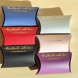 May include: Six pillow boxes in different colors, each with a gold sticker that says "handmade with love" and the website "BY TWOCREWDESIGN.COM".