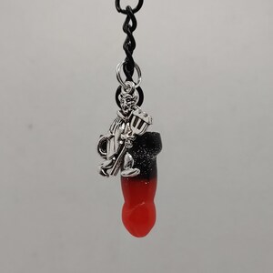 May include: A black and red candy shaped like a finger with a silver charm of a devil holding a pitchfork attached to a black keychain.