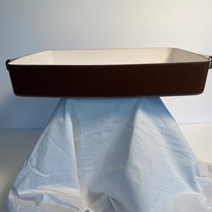 May include: A brown rectangular baking dish with white enamel interior. The dish has two handles on the sides.