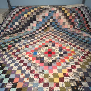 May include: A large patchwork quilt featuring a grid of numerous small fabric squares in a wide variety of colors, including red, blue, yellow, pink, and black, with diverse patterns such as floral, plaid, striped, and solid designs.