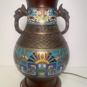 May include: An antique table lamp with a brown base and a decorative vase-shaped body. The lamp features colorful enamel designs in blue, red, yellow, and green. The lamp has two dragon-shaped handles and measures approximately 20 inches tall.
