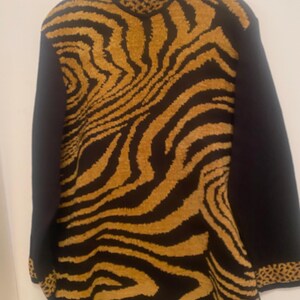 May include: A long-sleeved sweater with a bold zebra stripe pattern in shades of brown and black. The sleeves and collar are solid black, with a leopard print trim on the collar and cuffs. The sweater is hanging on a hanger.