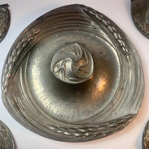 May include: A silver metal tray with a decorative design of wheat stalks around the edge. The tray has a smaller, circular dish in the center with a similar wheat stalk design.