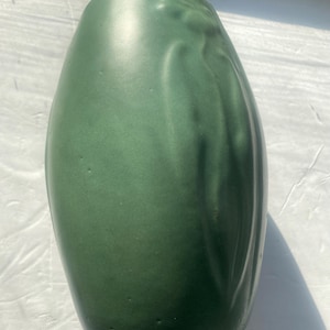 May include: A green ceramic vase with a textured, floral design. The vase is tall and slender, with a rounded bottom and a slightly flared opening.