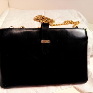 May include: A black leather handbag with a gold chain strap. The rectangular bag has a flap closure with a gold-tone accent. The bag is set against a white background.