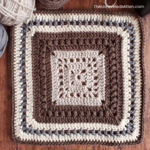 May include: A crocheted square with a brown, beige, and gray color scheme. The square has a detailed pattern with a central motif and a border.