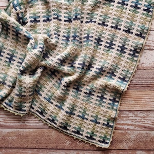 May include: A crocheted blanket with a geometric pattern in shades of green, blue, and white. The blanket has a crocheted border with a scalloped edge.